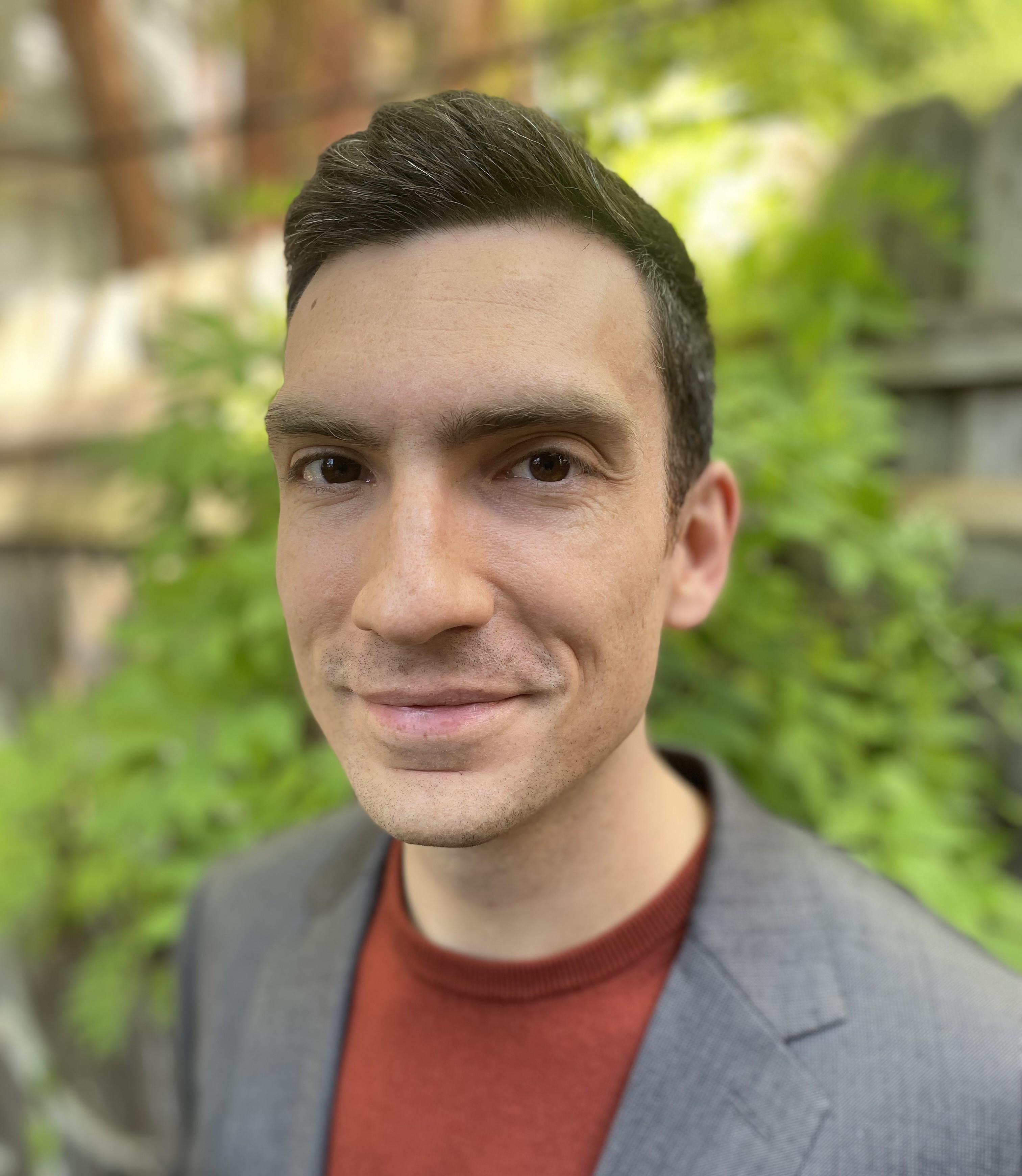 Headshot of Nick Graetz in a grey suit jacket and red sweater standing outside