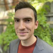 Headshot of Nick Graetz in a grey suit jacket and red sweater standing outside